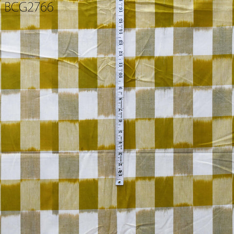 a fabric with a yellow and white checkered pattern, with a ruler placed vertically on it. The ruler is marked with measurements in inches.