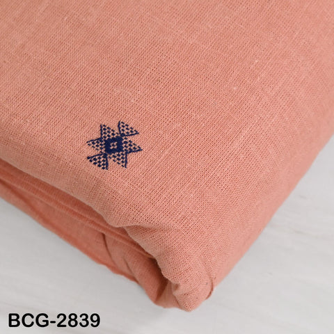 a close-up view of a peach-colored fabric with a small blue embroidered design on it.