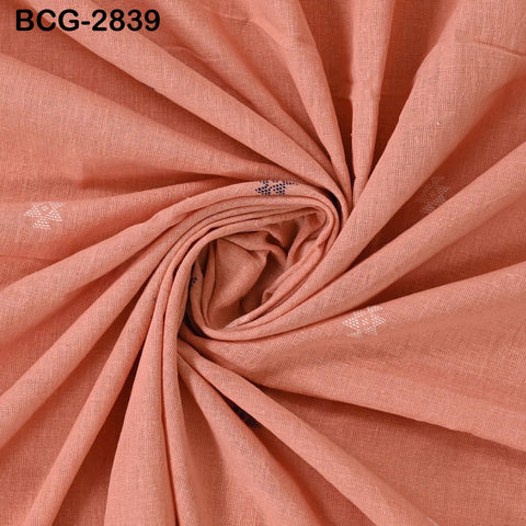 a close-up view of a fabric with a pinkish-orange hue, featuring a subtle pattern of small white flowers or dots. The fabric appears to be folded or twisted in a way that creates a sense of movement and texture.