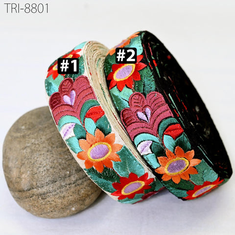 three colorful fabric rolls with floral patterns, including red, green, and orange flowers, placed on a white surface next to a rock.