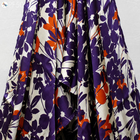 a close-up view of a fabric with a floral pattern in shades of purple and orange. The fabric appears to be a piece of clothing, possibly a dress or skirt, with a vibrant and eye-catching design.