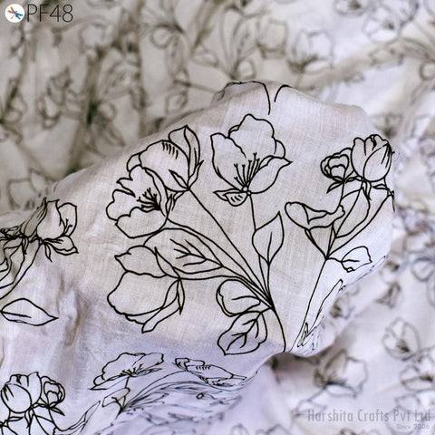 a close-up view of a fabric with a floral pattern, including various types of flowers and leaves. The fabric appears to be a white material with black outlines, creating a visually striking contrast. The image does not contain any text or additional objects, and the focus is solely on the intricate floral design on the fabric.