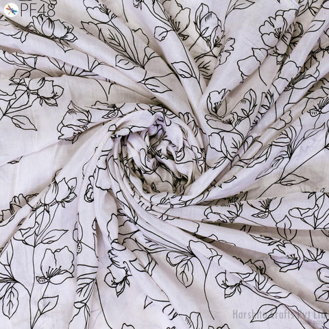 a close-up view of a fabric with a floral pattern, featuring black outlines of flowers and leaves. The fabric appears to be white, and the pattern is intricate and detailed.