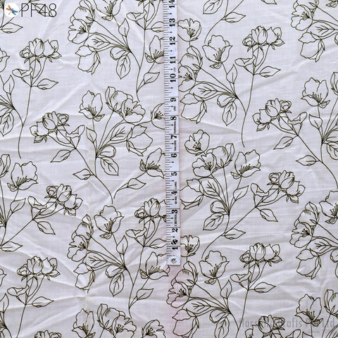 a close-up view of a fabric with a repeating floral pattern. The fabric appears to be white and features a black and white floral design. A ruler is placed vertically in the center of the fabric, likely for measuring purposes.