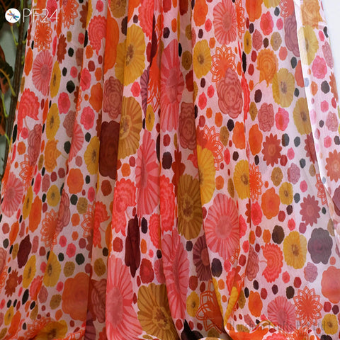a close-up view of a fabric with a vibrant floral pattern in shades of orange, pink, and yellow. The pattern is composed of various flowers and leaves, creating a visually striking and colorful design.