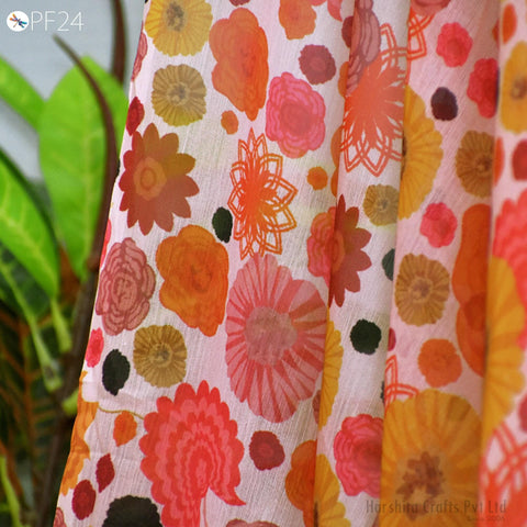 a close-up view of a fabric with a vibrant floral pattern, including various shades of orange, pink, and yellow flowers. The fabric appears to be a sheer material, with a white background that highlights the colorful design.