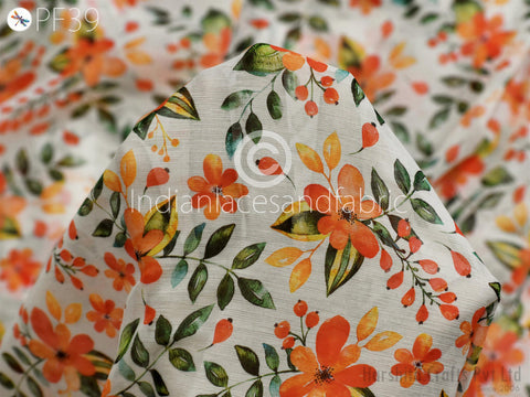 a close-up view of a fabric with a floral pattern, including orange and green leaves and flowers. The fabric appears to be a white material with a colorful, hand-painted design.
