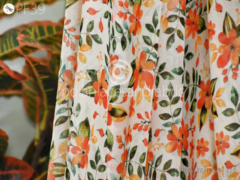 a close-up view of a fabric with a floral pattern, including orange and green flowers and leaves. The fabric appears to be a sheer material, with a white background.