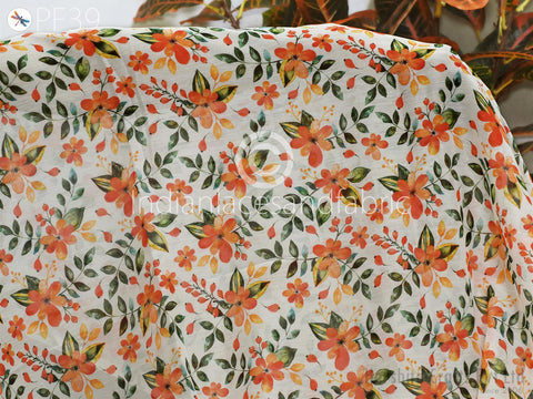a close-up view of a fabric with a floral pattern, including orange and green flowers and leaves. The fabric appears to be a white material with a colorful, hand-painted design.