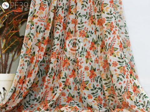 a close-up view of a fabric with a floral pattern in shades of orange and green. The fabric appears to be a sheer material, with a white background behind it.