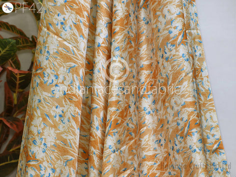 a close-up view of a fabric with a floral pattern in shades of orange and white. The fabric appears to be made of silk and is displayed against a white background.