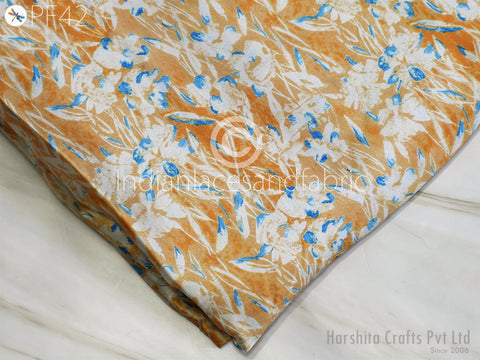 a close-up view of a fabric with a floral pattern in shades of orange and blue. The fabric appears to be folded or rolled up, and there is a watermark or logo visible in the bottom right corner.