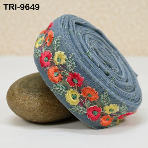 A blue fabric with colorful floral embroidery is displayed on a white surface, with a rock visible underneath it.