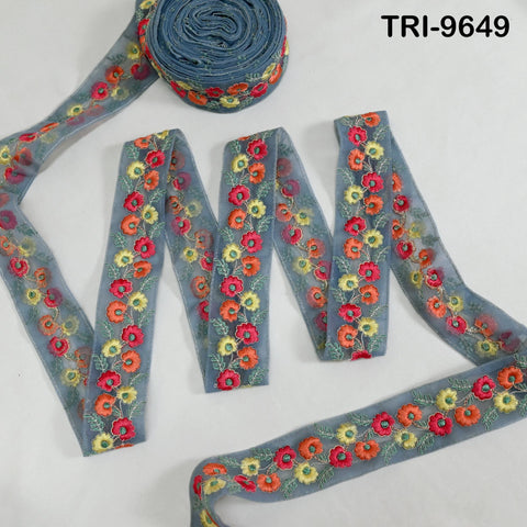 a collection of decorative fabric pieces, including a blue ribbon with a floral pattern and a spool of thread with a similar floral design.