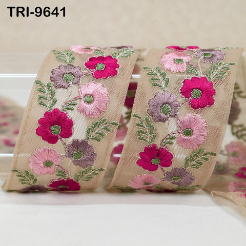 a close-up view of a decorative fabric with a floral pattern. The fabric is adorned with pink and purple flowers, along with green leaves, creating a visually appealing and intricate design.