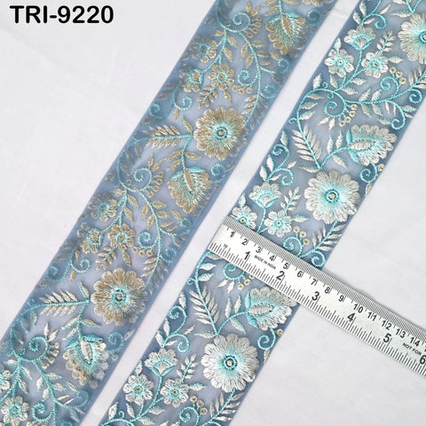 a close-up view of a decorative fabric with a floral pattern in shades of blue and gold. The fabric is laid out on a white surface, and a ruler is placed next to it, indicating the size of the fabric.