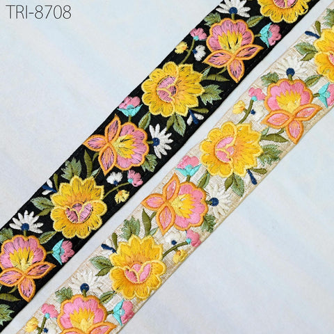 two spools of embroidered fabric with floral designs. The spools are placed side by side, with the left one appearing to be black and the right one being white. The spools have a colorful and intricate floral pattern, featuring yellow and pink flowers along with green leaves. The spools are positioned on a white surface, which highlights their vibrant colors and designs.