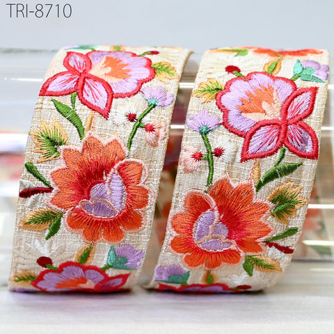 two rolls of fabric with vibrant floral embroidery, including red, pink, and orange flowers, along with green leaves and stems.