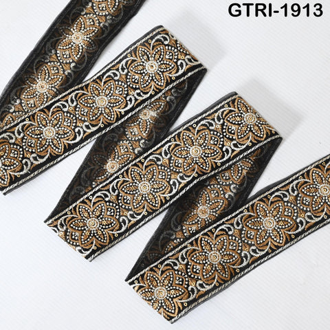 a decorative fabric with a floral pattern in shades of black and gold. The fabric appears to be a decorative trim or border, with a repeating floral design.