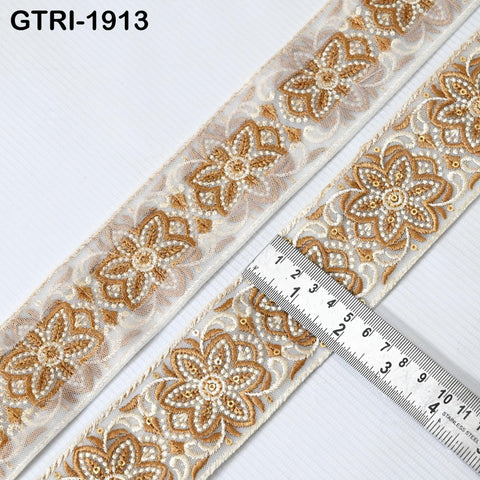 a close-up view of a decorative fabric with a repeating pattern of gold and white floral designs. A ruler is placed on the fabric, indicating the size or dimensions of the pattern.