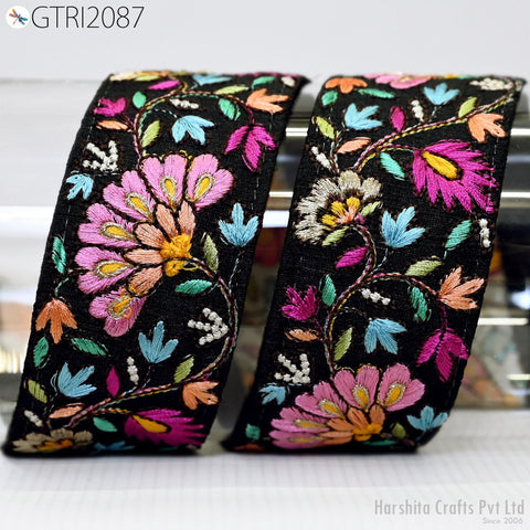 two decorative fabric pieces with a floral pattern in shades of pink, orange, and green. The fabric appears to be black, with the intricate embroidery and floral designs adding a vibrant touch to the overall appearance.