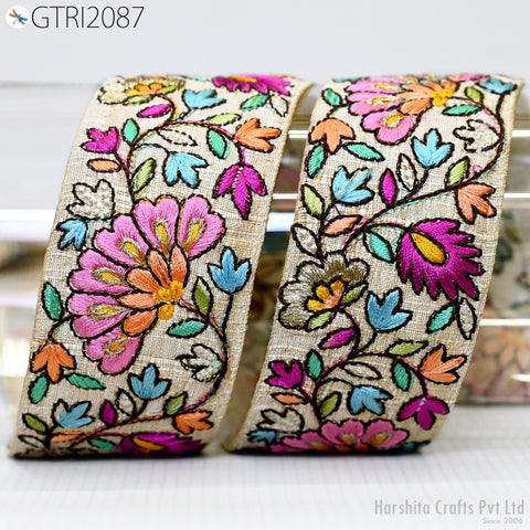 two rolls of embroidered fabric with a floral pattern. The fabric has a beige color and is adorned with colorful flowers and leaves in shades of pink, orange, blue, and green. The rolls are placed side by side, showcasing the intricate and vibrant embroidery work.