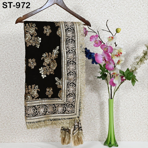 a black and gold embroidered shawl hanging on a wooden hanger, with a vase of pink and white flowers placed next to it on a white surface.