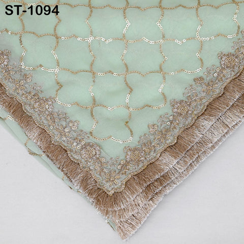 a close-up view of a decorative fabric with a light green background and gold sequin and fringe details.