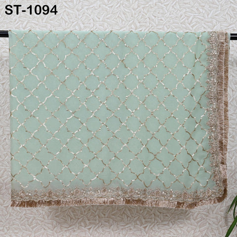 a light green fabric with a gold and white diamond pattern, hanging on a wall. The fabric appears to be a decorative textile, possibly a shawl or a blanket.
