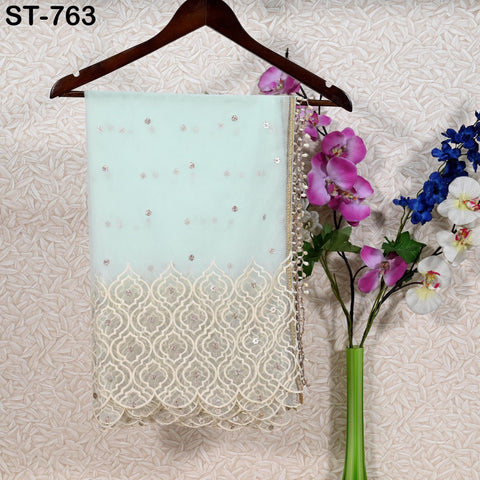 a light blue fabric with a lace-like pattern, hanging on a wooden hanger. Next to the fabric, there is a green vase with purple and white flowers. The background has a patterned wallpaper.