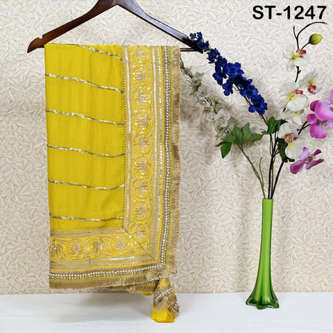 a yellow and gold sari hanging on a wooden hanger, with a vase of flowers placed next to it on a table.