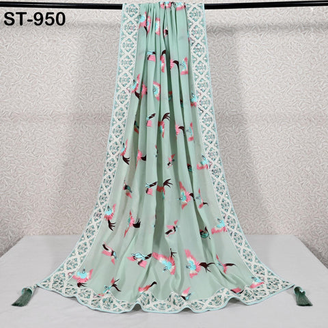 a light green fabric with a floral pattern, hanging on a white surface. The fabric has a decorative border and tassels at the bottom.