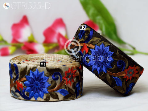 two decorative fabric pieces with intricate floral patterns in shades of blue and brown. The fabric pieces are placed on a white surface, with a blurred background that includes pink and green flowers.
