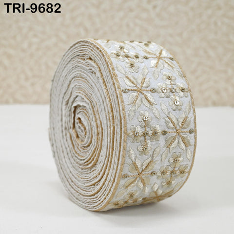 A close-up image of a decorative fabric with a floral pattern, featuring a white and gold color scheme.