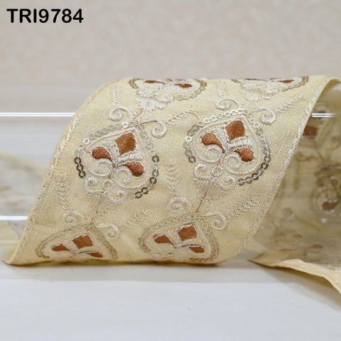 a close-up view of a decorative fabric with intricate embroidered patterns in shades of beige and brown.
