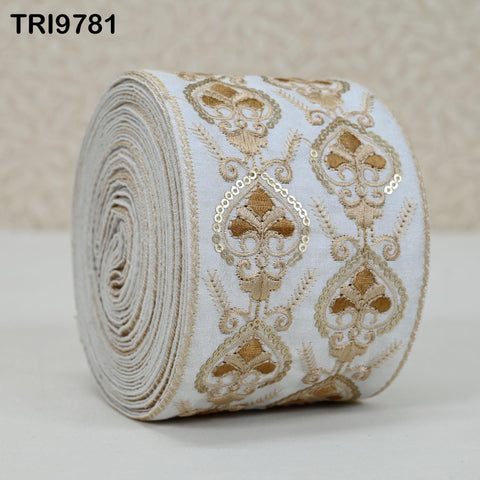 A roll of white fabric with gold embroidered designs, including floral and leaf motifs, is displayed against a light background.