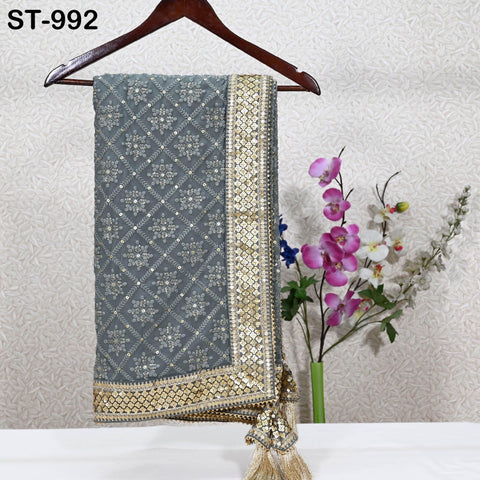 a grey and gold embroidered shawl hanging on a wooden hanger, with a vase of pink and purple flowers placed next to it on a table.
