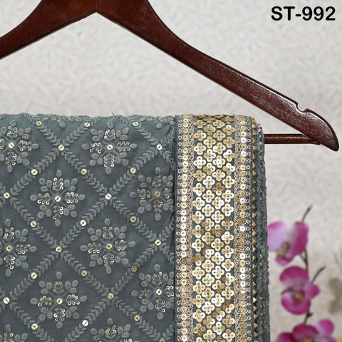 a grey fabric with a gold and silver sequin trim, hanging on a wooden hanger. The background features a floral pattern.