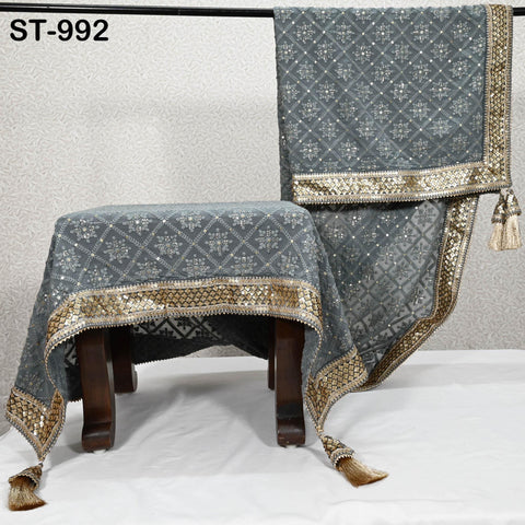 a gray and gold patterned fabric with a tassel hanging from the bottom, placed on a white surface.