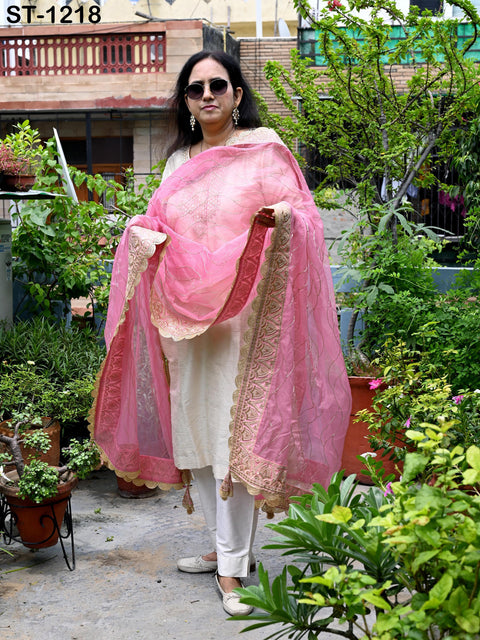 A woman wearing a pink and white outfit stands in a garden surrounded by potted plants.
