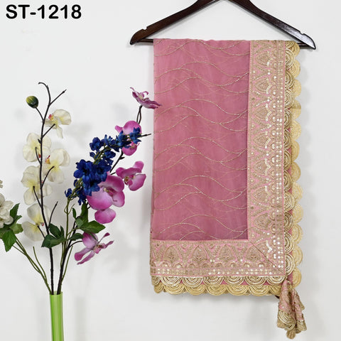 a pink fabric with gold trim, hanging on a wooden hanger. Next to the fabric, there is a vase with purple and white flowers.