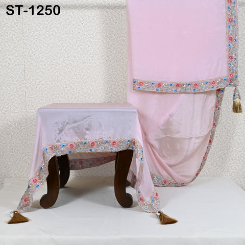 a pink fabric with a floral pattern and tassels, displayed on a wooden stand.