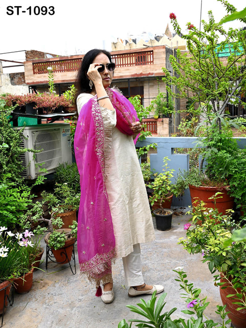 A woman in a white and pink dress stands in a garden surrounded by potted plants and flowers.