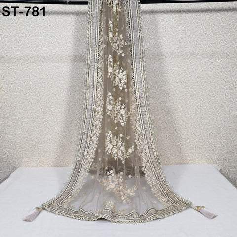 a long, ornate, and intricately designed fabric draped over a white surface. The fabric has a floral pattern and is adorned with tassels at the bottom. The background is a white wall with a patterned design.