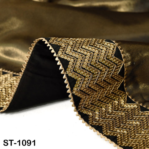 a close-up view of a piece of fabric with a gold and black zigzag pattern, featuring a black border and a gold-colored border. The fabric appears to be made of silk or a similar material, and the image is taken from a side angle.