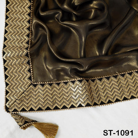 a close-up view of a shiny, dark fabric with a gold and black zigzag pattern along the border. The fabric appears to be made of silk or satin, and the border is embellished with sequins or sequin-like material. The image does not contain any text or additional objects.