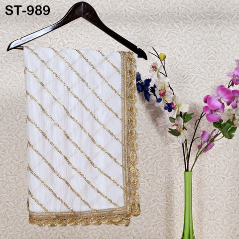 a white and gold embroidered scarf hanging on a wooden hanger, with a vase of purple and pink flowers placed next to it on a wall.