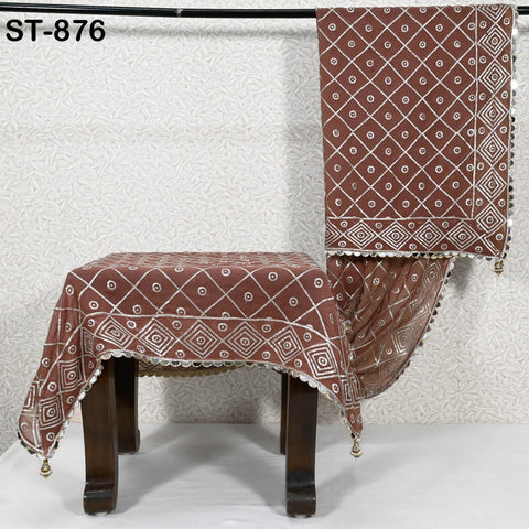 a brown tablecloth with a diamond pattern and a matching blanket draped over it, both hanging on a wooden stand against a white wall.
