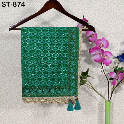 a green and gold sequined saree hanging on a wooden hanger, with a vase of pink orchids placed next to it on a wall.