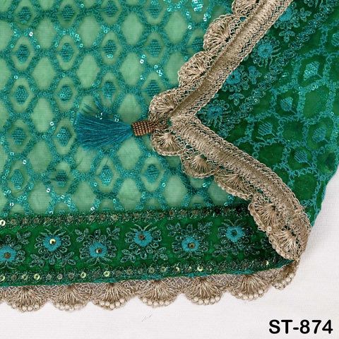 a close-up view of a fabric with a green and blue pattern, featuring intricate embroidery and a tassel. The fabric appears to be a textile or garment, with a decorative border and trim.